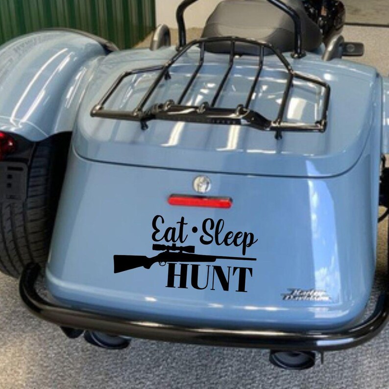 May include: A light blue motorcycle with a black luggage rack and bumper. The words "Eat Sleep HUNT" are displayed in black, along with a rifle graphic.