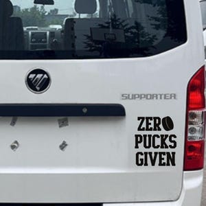 May include: White vehicle rear with a black decal. The decal reads "ZERO PUCKS GIVEN" with a hockey puck graphic. The vehicle also has a red tail light and a black handle.