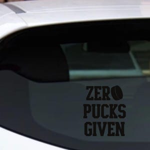 May include: Black vinyl decal with the words "ZERO PUCKS GIVEN" and a hockey puck graphic. The decal is applied to the rear window of a vehicle.