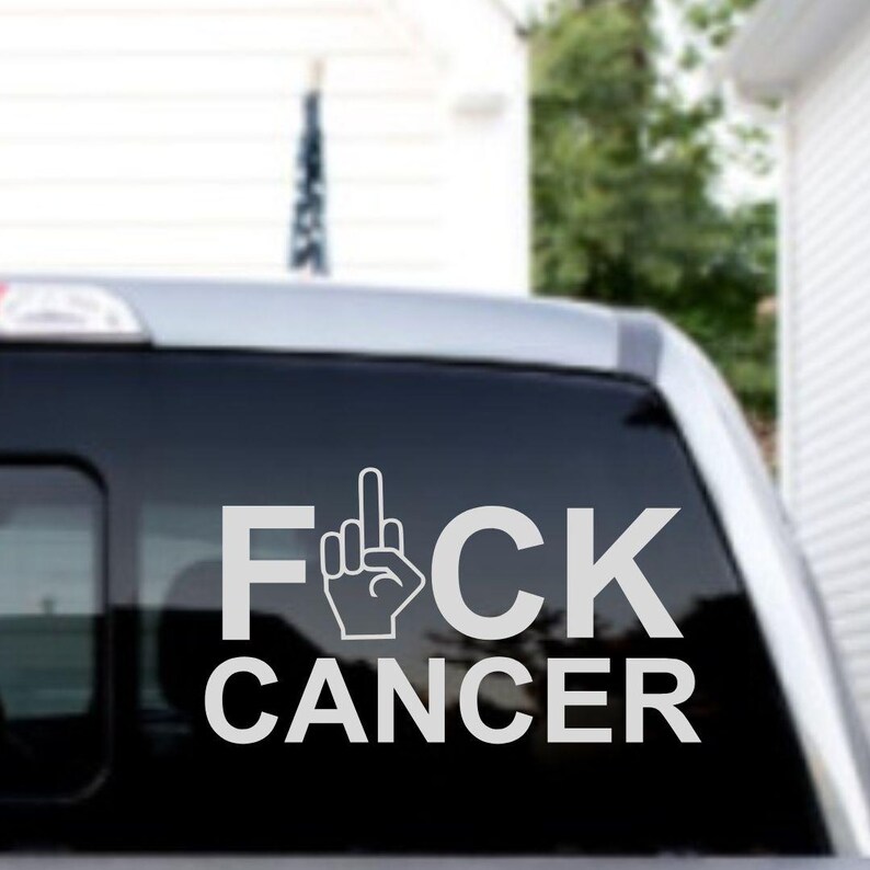 May include: A white decal with the words "F*CK CANCER" and a middle finger symbol on a black car window.