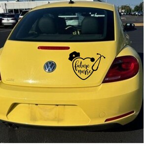 May include: A yellow car with a black decal on the back window. The decal is a heart with a stethoscope and a nurse's cap. The text inside the heart says "future nurse".