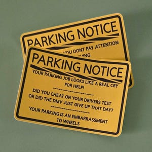 May include: Two yellow parking notice signs with black text. The signs read "PARKING NOTICE" at the top, followed by humorous statements about parking skills. The signs are rectangular with rounded corners.