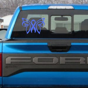 May include: A blue butterfly-shaped decal with a blue ribbon in the center. The decal is on the back window of a blue pickup truck.