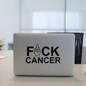 May include: A black and white sticker on a silver laptop that says "F*CK CANCER" with a middle finger emoji.
