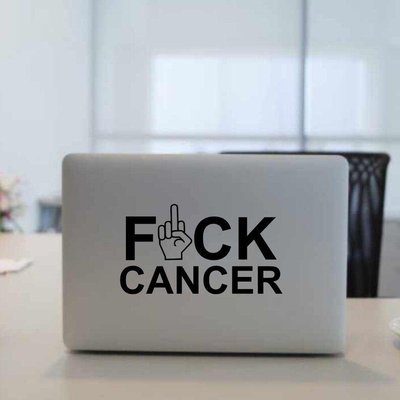 May include: A black and white sticker on a silver laptop that says "F*CK CANCER" with a middle finger emoji.