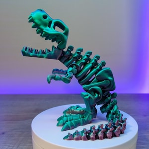 May include: A 3D printed dinosaur skeleton figurine with a green iridescent finish. The dinosaur is posed standing on a white circular base.