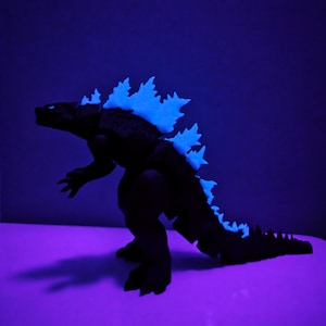 Könnte beinhalten: Eine schwarze Godzilla-Actionfigur mit einer blau leuchtenden Rückenflosse. Die Figur steht in einer stehenden Position mit ausgestrecktem Schwanz.