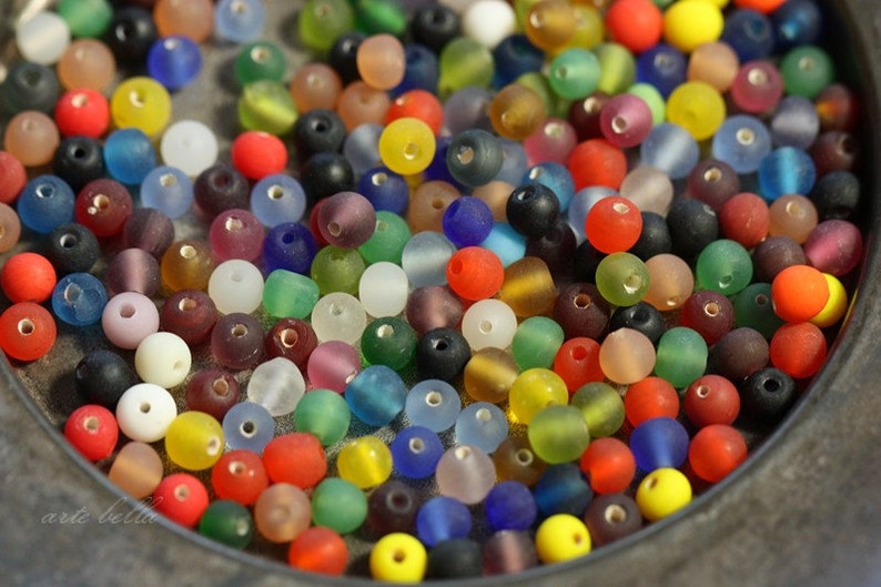 May include: A bowl filled with a variety of colorful glass beads. The beads are opaque and have a frosted finish. They are in a range of colors, including red, blue, green, yellow, and purple.