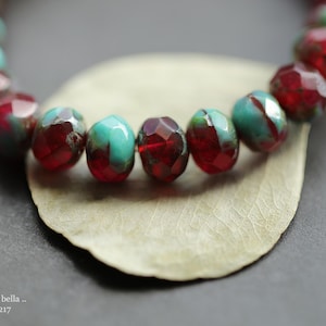 May include: A close-up of a bracelet made of red and turquoise faceted beads. The beads are arranged in a circular pattern and are strung on a clear elastic cord.