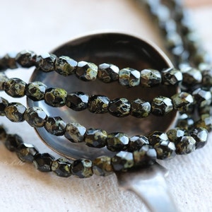May include: A strand of black and green faceted glass beads. The beads have a speckled, marbled appearance.