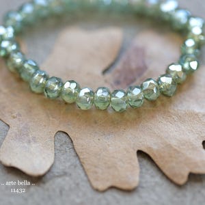 May include: A pale green beaded bracelet with faceted beads. The bracelet is displayed on a brown leaf. The image includes the text ".. arte bella .." and "11432".