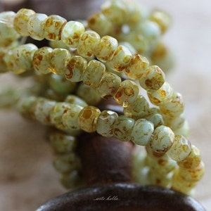 May include: A strand of light green glass beads with a brown marbled pattern. The beads are faceted and have a slightly irregular shape.