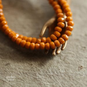 May include: A close-up of a long strand of orange glass beads. The beads are faceted and have a glossy finish. The beads are arranged in a circular pattern, creating a decorative effect.