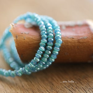 May include: A close-up of a blue glass bead necklace wrapped around a piece of driftwood. The beads are iridescent and have a slightly textured surface.