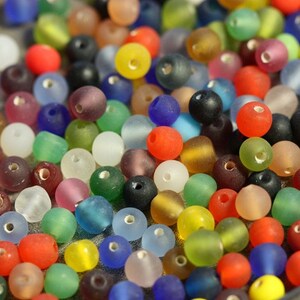 May include: A close-up of a variety of colorful glass beads. The beads are round and have a frosted finish. They are arranged in a random pattern.