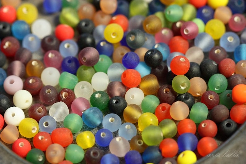 May include: A close-up of a variety of colorful glass beads. The beads are round and have a frosted finish. They are arranged in a random pattern.