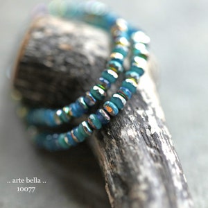 May include: A close-up of a blue and silver beaded bracelet on a piece of driftwood. The beads are iridescent and have a faceted finish.