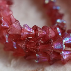May include: Close-up of a strand of translucent, pink flower-shaped beads. The beads have an iridescent sheen, reflecting multiple colors. The beads are arranged in a curved line, suggesting they are part of a necklace or bracelet.