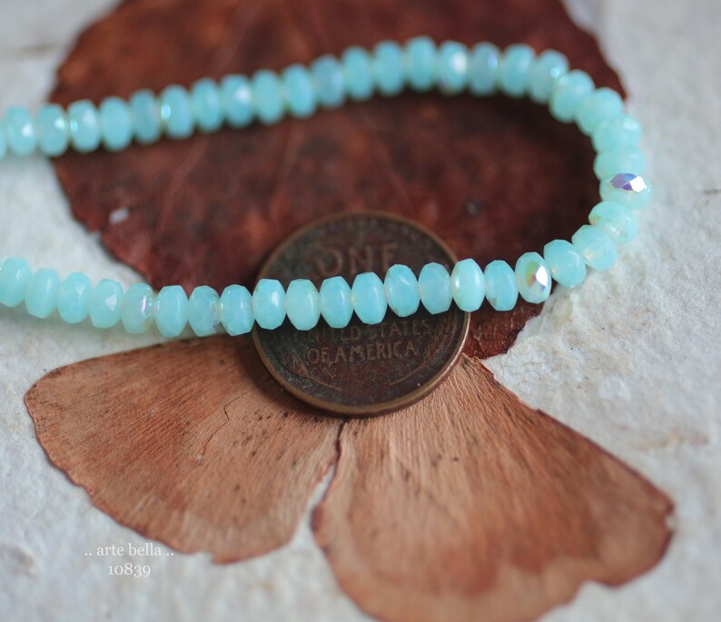 May include: A light blue beaded bracelet made of faceted glass beads. The bracelet is lying on a brown and white surface.