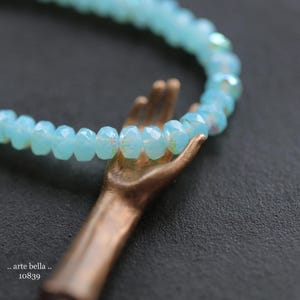 May include: A delicate bracelet made of light blue faceted glass beads. The bracelet is held by a hand-shaped bronze charm.