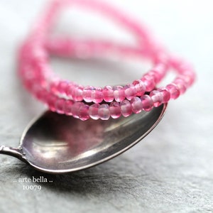 May include: A pink beaded bracelet made of small, faceted beads. The bracelet is lying on a silver spoon.