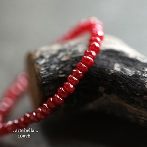 May include: A red gemstone bracelet with faceted beads. The bracelet is on a piece of wood.