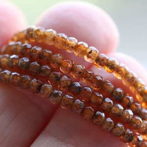 May include: A strand of brown gemstone beads with a faceted finish. The beads are small and round, and they are strung together on a clear thread.