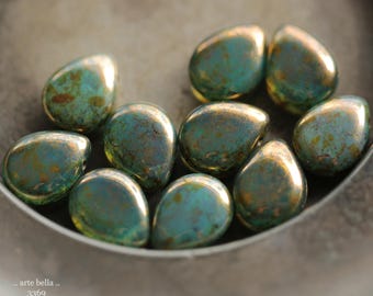 May include: A collection of ten teardrop-shaped beads with a metallic, iridescent finish in shades of teal, green, and bronze. The beads feature a smooth, polished surface with mottled color variations. Text in the corner reads: .. arte bella .. 3369.