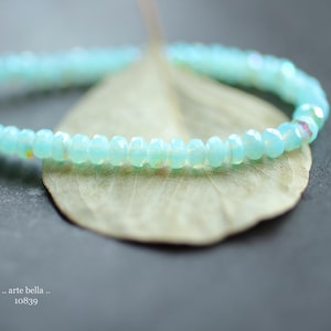 May include: A delicate bracelet made of light blue beads. The bracelet is lying on a light brown leaf.
