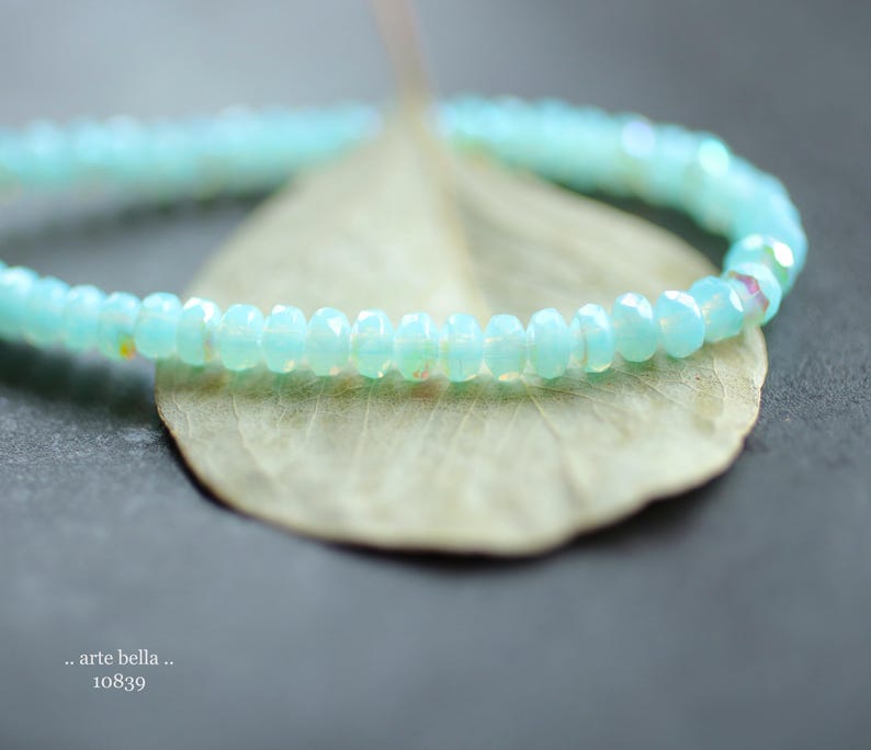 May include: A delicate bracelet made of light blue beads. The bracelet is lying on a light brown leaf.