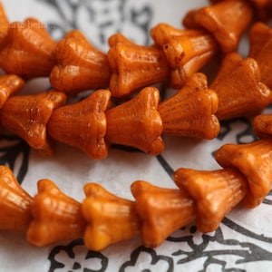 May include: A string of orange bell-shaped beads. The beads are made of a smooth, slightly textured material.