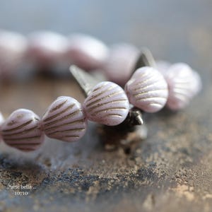 May include: A strand of pink glass beads with a shell-like design. The beads have a subtle shimmer and are strung on a silver wire.