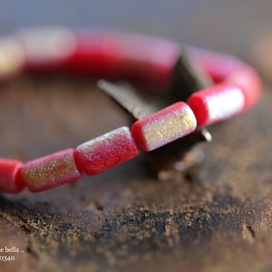 Könnte beinhalten: Nahaufnahme eines roten und goldenen Armbands mit einem silbernen Verschluss. Das Armband besteht aus kleinen, rechteckigen Perlen.