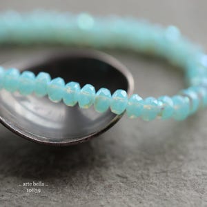 May include: A light blue beaded bracelet with a delicate, iridescent finish. The bracelet is made of small, round beads that are strung together to create a simple, elegant design.