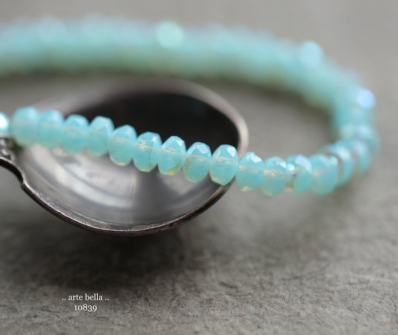 May include: A light blue beaded bracelet with a delicate, iridescent finish. The bracelet is made of small, round beads that are strung together to create a simple, elegant design.