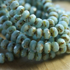 May include: A strand of light blue glass beads with brown flecks. The beads are faceted and have a slightly irregular shape.