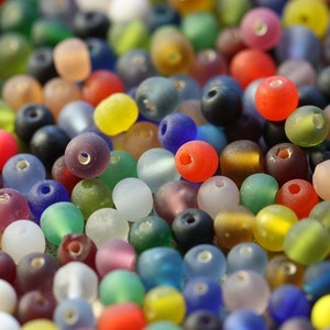 May include: A large assortment of colorful glass beads in various shapes and sizes. The beads are frosted and have a translucent appearance.