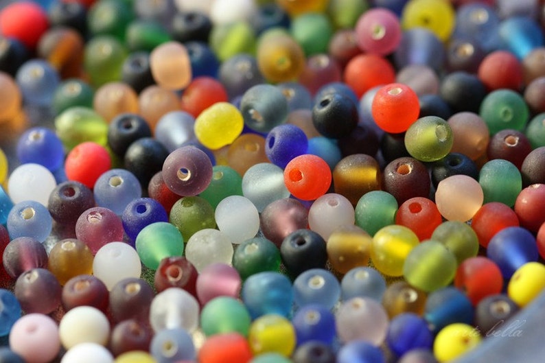 May include: A large assortment of colorful glass beads in various shapes and sizes. The beads are frosted and have a translucent appearance.