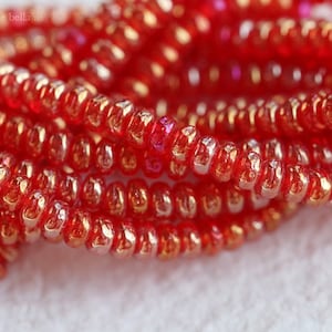 May include: A strand of red glass beads with a metallic sheen. The beads are small and round, and they are strung together on a clear thread.
