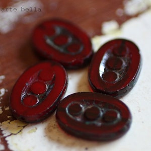May include: Four dark red glass beads with a raised design of three circles. The beads are oval shaped and have a glossy finish.