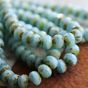 May include: Strands of light blue beads with brown and yellow accents. The beads are round and have a glossy finish. The beads are strung together, creating a necklace or bracelet.