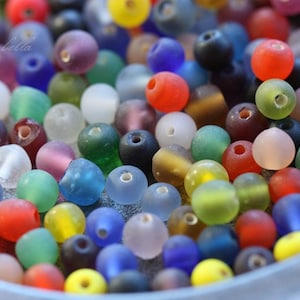May include: A collection of colorful glass beads in various shades of blue, green, red, purple, and white. The beads are smooth and have a frosted finish.