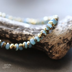 May include: A close-up of a blue and gold beaded bracelet on a piece of driftwood. The beads are faceted and have a metallic sheen.