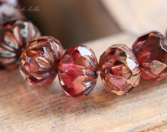 May include: Close-up of several faceted, oval-shaped beads. The beads are a deep red color with hints of brown and blue, and have a geometric pattern. The beads are strung together, suggesting they are for jewelry making.