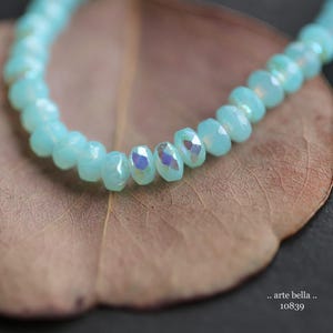 May include: A strand of light blue iridescent beads on a brown leaf background.