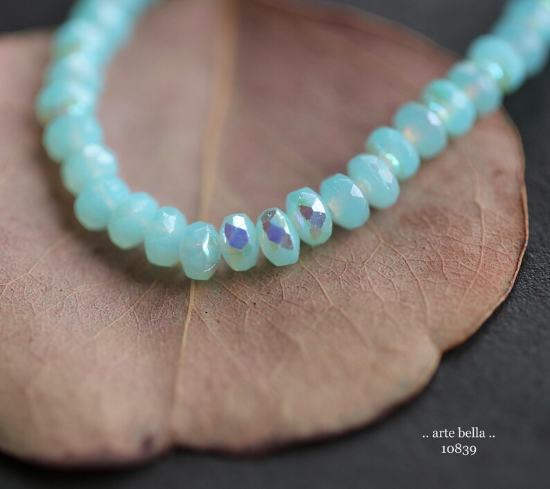 May include: A strand of light blue iridescent beads on a brown leaf background.