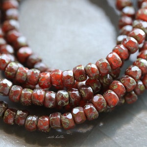May include: A strand of red glass beads with a speckled, textured surface. The beads are faceted and have a slightly irregular shape.