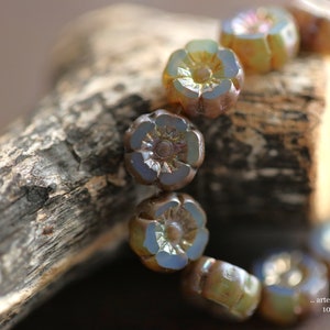 May include: A strand of iridescent glass beads in the shape of flowers. The beads are a mix of light blue, purple, and brown.