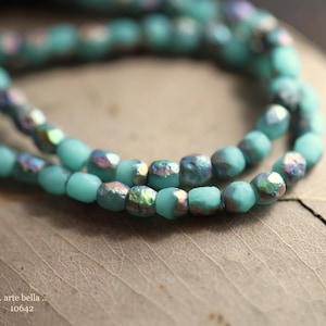 May include: A strand of turquoise blue glass beads with iridescent accents. The beads are faceted and have a slightly irregular shape.
