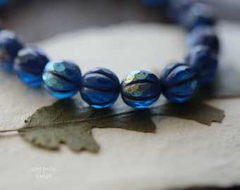 May include: A close-up of a blue glass bead necklace with a textured surface. The beads are round and have a metallic sheen.